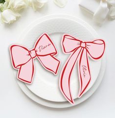 two pink bows on a white plate next to flowers and napkins with the word mom written on them