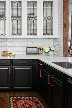 a kitchen with black cabinets and white subway backsplashes, an area rug in front of the sink