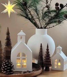 small white houses are sitting on a tray with pine cones and evergreen branches in the background