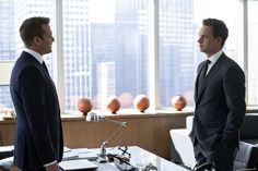 two men in suits are standing near a desk