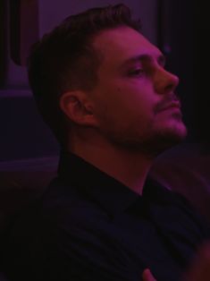 a man sitting in a dark room with his hand on his chest looking off to the side