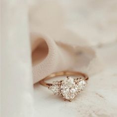 an engagement ring with three pear shaped diamonds on it, sitting next to a white cloth