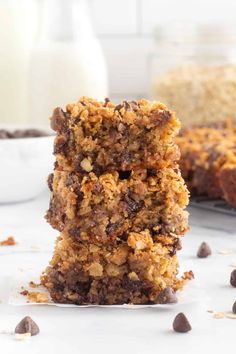 two pieces of chocolate chip cookie bars stacked on top of each other with milk in the background