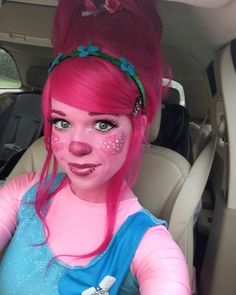 a woman with pink hair and blue dress sitting in a car