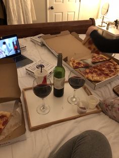 pizza and wine are sitting on the bed in front of a laptop computer, which is open