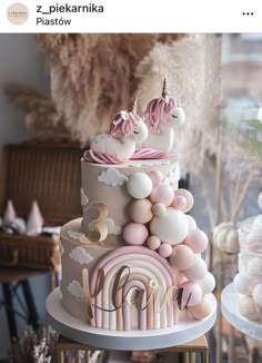 a three tiered cake decorated with pink and white icing, unicorn figurines and balloons