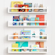 three white shelves with books on them against a wall in a children's room