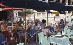 people sitting at tables under umbrellas in an outdoor cafe area with blue and white tablecloths