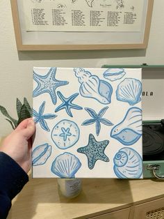 a person holding up a piece of paper with shells and starfishs on it