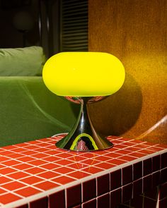 a yellow table lamp sitting on top of a red tiled counter next to a green couch