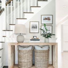 two wicker baskets under a table in front of a staircase with pictures on the wall