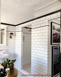 a white tiled bathroom with pictures on the wall and shower stall in the corner, along with potted plants