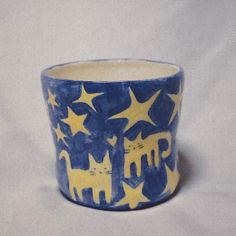 a blue and yellow cup with cats on it's sides sitting on a white surface