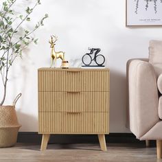 a small wooden dresser next to a chair and potted plant in a living room