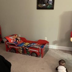 a toddler sitting on the floor in front of a firetruck toy box