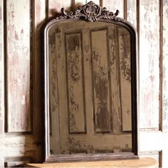 an old mirror hanging on the wall in front of a wooden paneled door with peeling paint