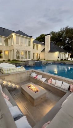 an outdoor fire pit in the middle of a backyard with couches and tables around it