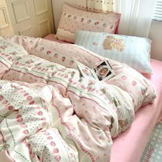 an unmade bed with pink and white sheets, pillows and a teddy bear on it