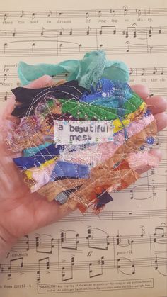 a person's hand holding a bunch of colorful pieces of cloth and paper on top of sheet music