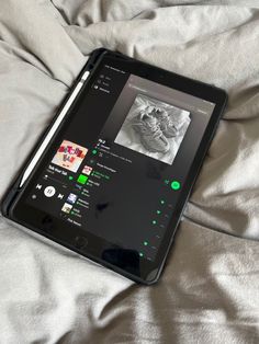 an ipad sitting on top of a bed covered in white sheets with green and black buttons