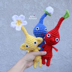 hand holding three crocheted stuffed animals in different colors