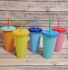 four different colored cups with straws in them on a wooden table next to wood planks