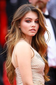 a woman with long brown hair wearing a white dress and posing for the camera at an event