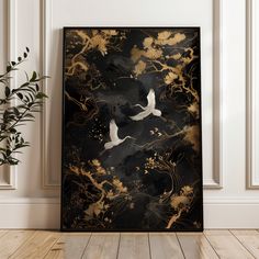 a black and gold painting with two white birds flying over the trees in front of it