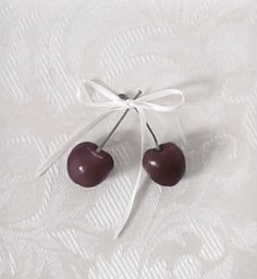 two cherries tied to a white ribbon on top of a bed sheet with an ornament