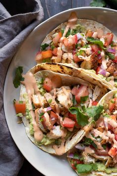 three fish tacos on a plate with guacamole, tomatoes and cilantro