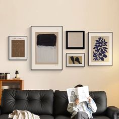 a woman sitting on top of a black couch next to a wall covered in pictures