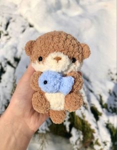 a hand holding a small teddy bear in the snow