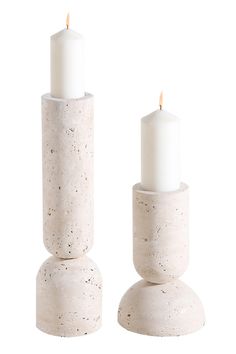 two white candles sitting on top of each other next to each other in concrete holders