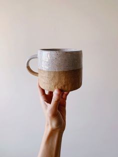 a hand holding up a coffee cup in front of a white wall