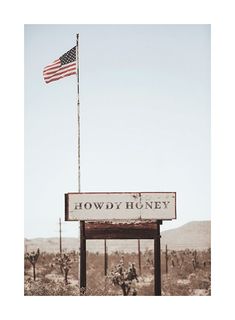 an american flag flying over a sign that reads lowy huny in front of a desert landscape