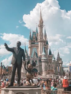 a statue of walt and mickey mouse in front of a castle with people around it