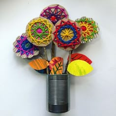 a vase filled with colorful paper flowers sitting on top of a white table next to a can