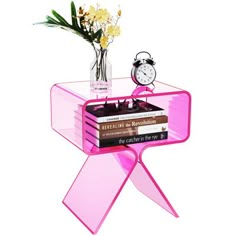 a pink end table with books and a clock on top, sitting next to a vase filled with flowers