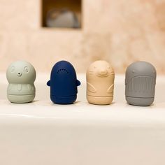 four different colored objects sitting on top of a bath tub next to a toilet paper dispenser