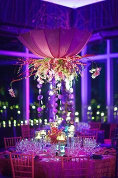 a table set up for a formal function with purple lighting and flowers in the center