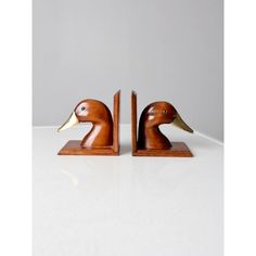 two wooden ducks are sitting side by side on a white counter top, one has its head turned to look like it's sticking out from behind the other