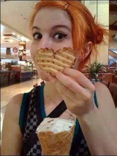 a woman with red hair is eating an ice cream cone and looking at the camera