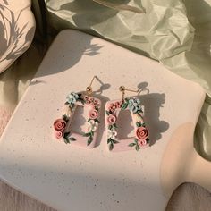 two pairs of earrings with flowers on them sitting on a table next to a pillow