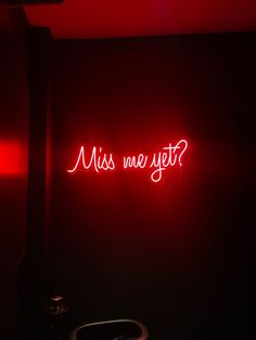 a red neon sign that says miss me yet? in the corner of a dark room