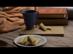 some food is on a plate next to a book and a coffee cup with a blue mug