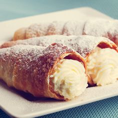 two pastries on a white plate covered in powdered sugar and cream sitting on a blue tablecloth