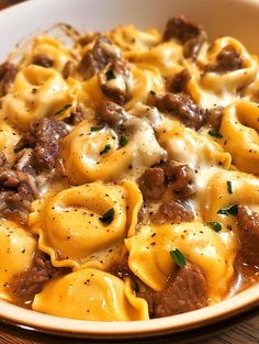 a bowl filled with pasta and meat on top of a wooden table next to a fork