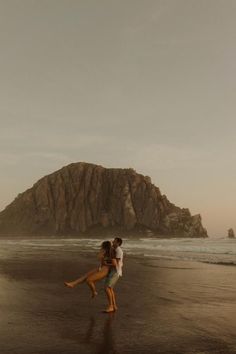 a man and woman are dancing on the beach with an island in the back ground