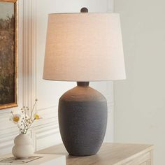 a table lamp sitting on top of a dresser next to a vase with flowers in it