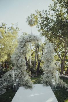 an outdoor wedding setup with white flowers and candles on the ground, surrounded by trees